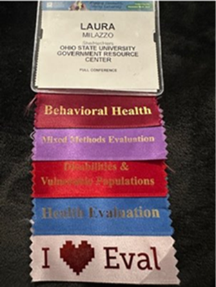 Laura's Evaluation 2025 name badge with five multicolored ribbons showing which presentations she attended (Behavioral Health, Mixed Methods Evaluation, Disabilities and Vulnerable Populations, Health Evaluation, and I Love Eval).