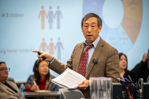 Male speaker standing in front of a large screen pointing to the presentation.