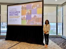 Brynne Presser Funderburg standing by the promotional screen for the 2024 AcademyHealth Annual Research Meeting (Today's Research driving Tomorrow's outcomes.)