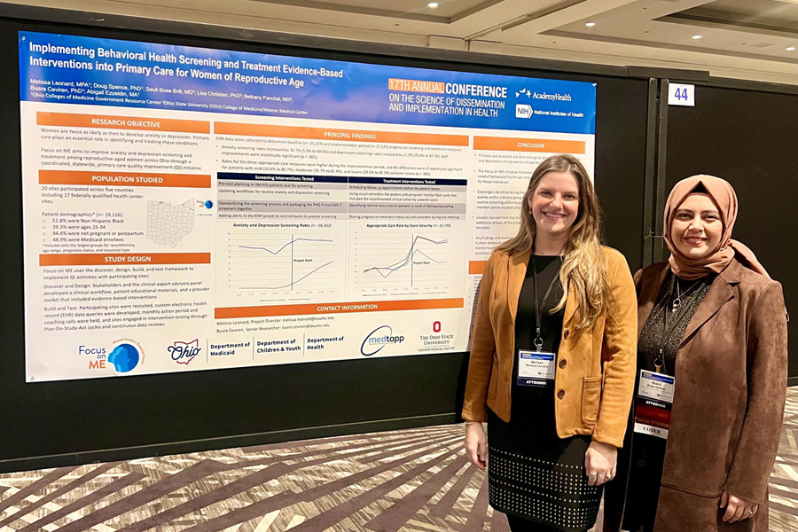 Melissa and Busra standing in front of their Focus on Me poster, smiling.