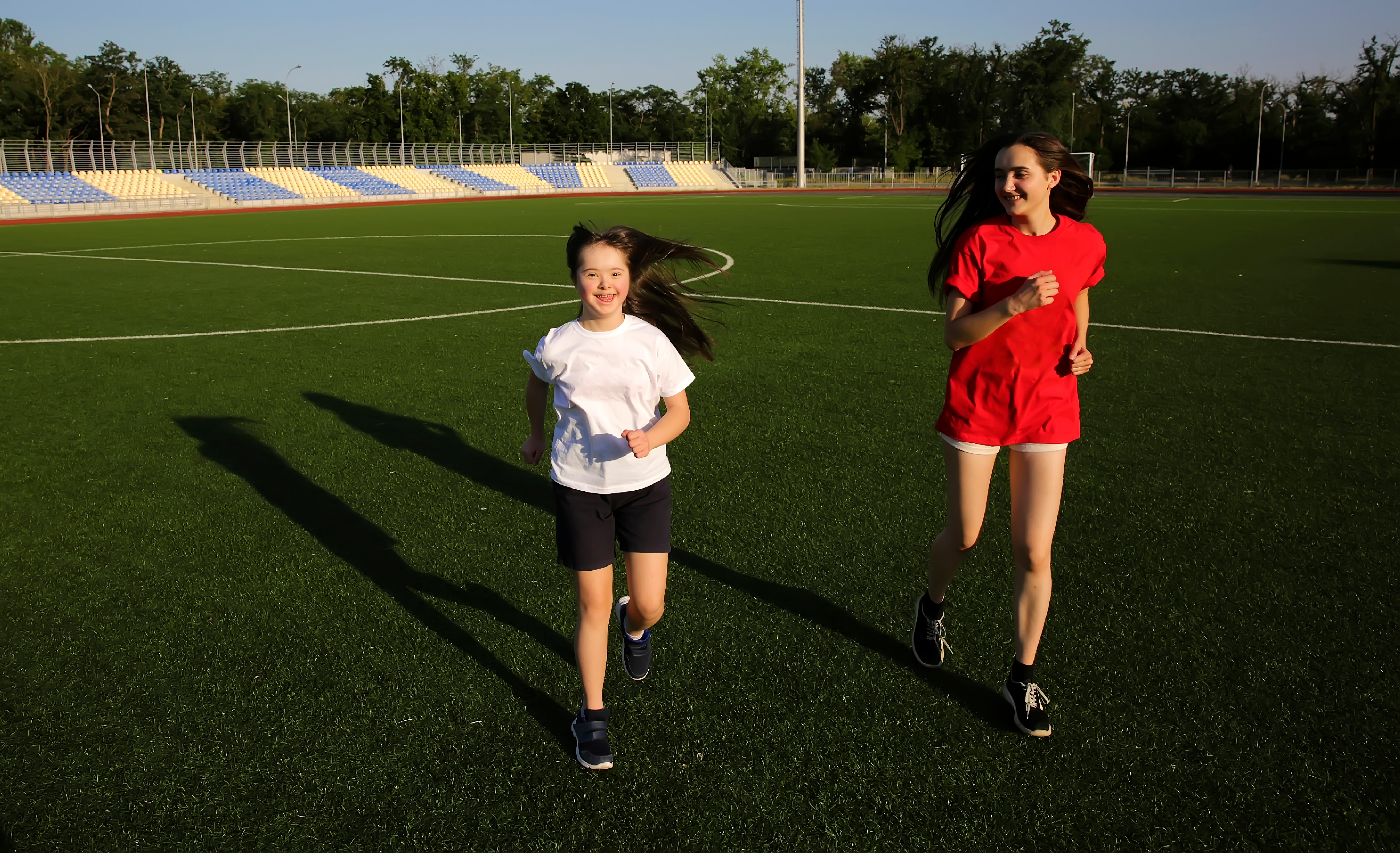 A young girl with a big smile, who identifies with Down Syndrome, is racing another girl who is also smiling.