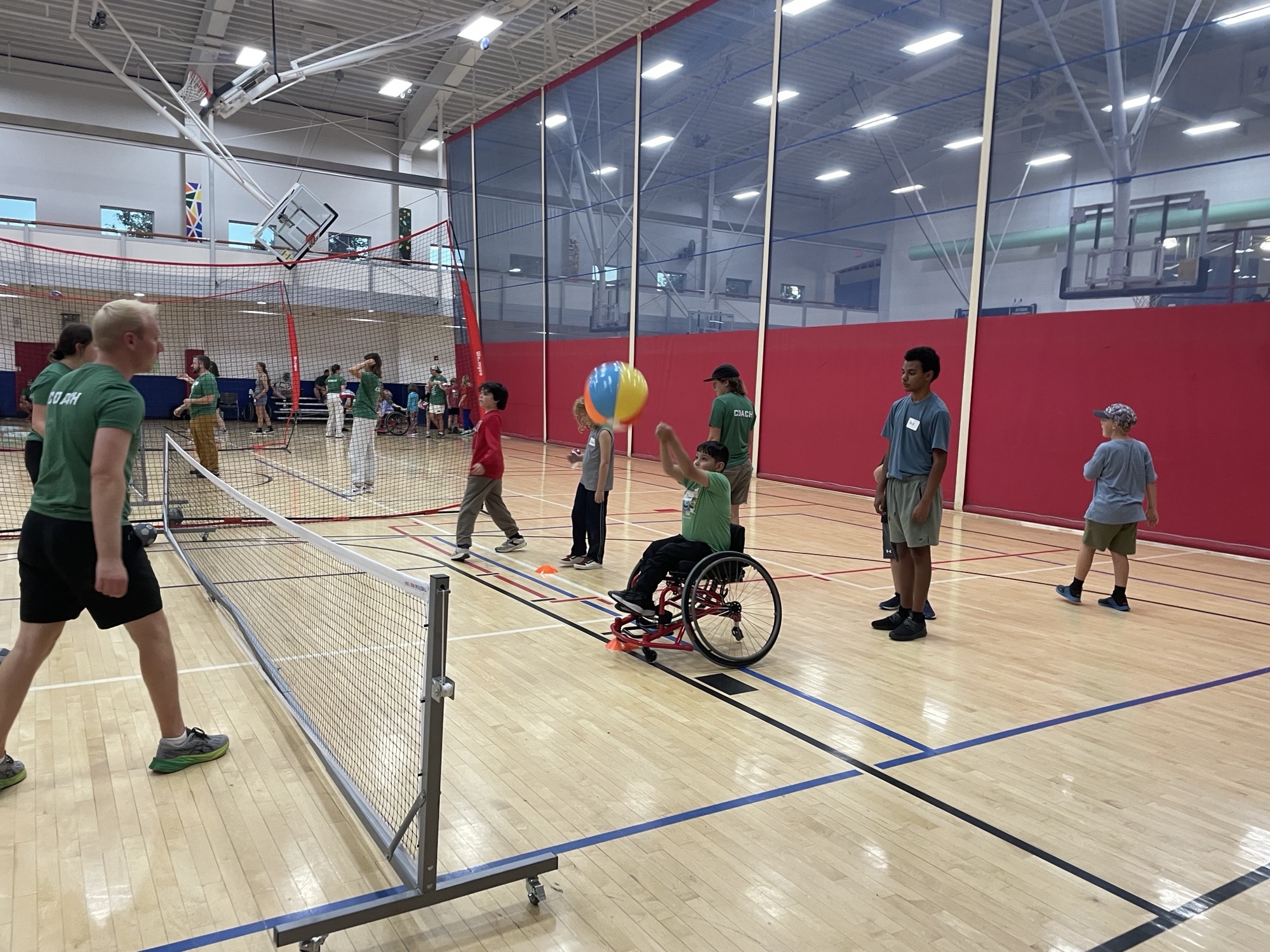 Group of youth with and without disabilities playing volleyball in an Athens gym with coaches