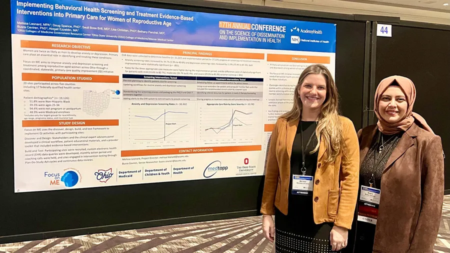 Melissa and Busra standing in front of their Focus on Me poster, smiling.