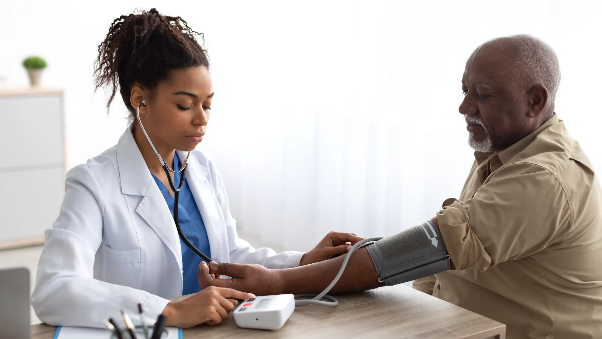 A female medical provider in a white coat takes the blood pressure of a patient.