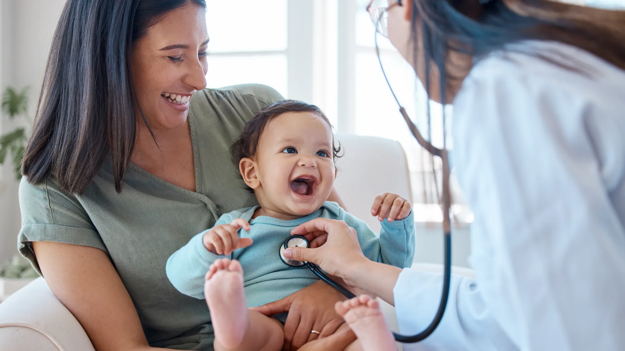 Laughing mom and baby in her lap with a clinician checking the baby's heartbeat with a steth.
