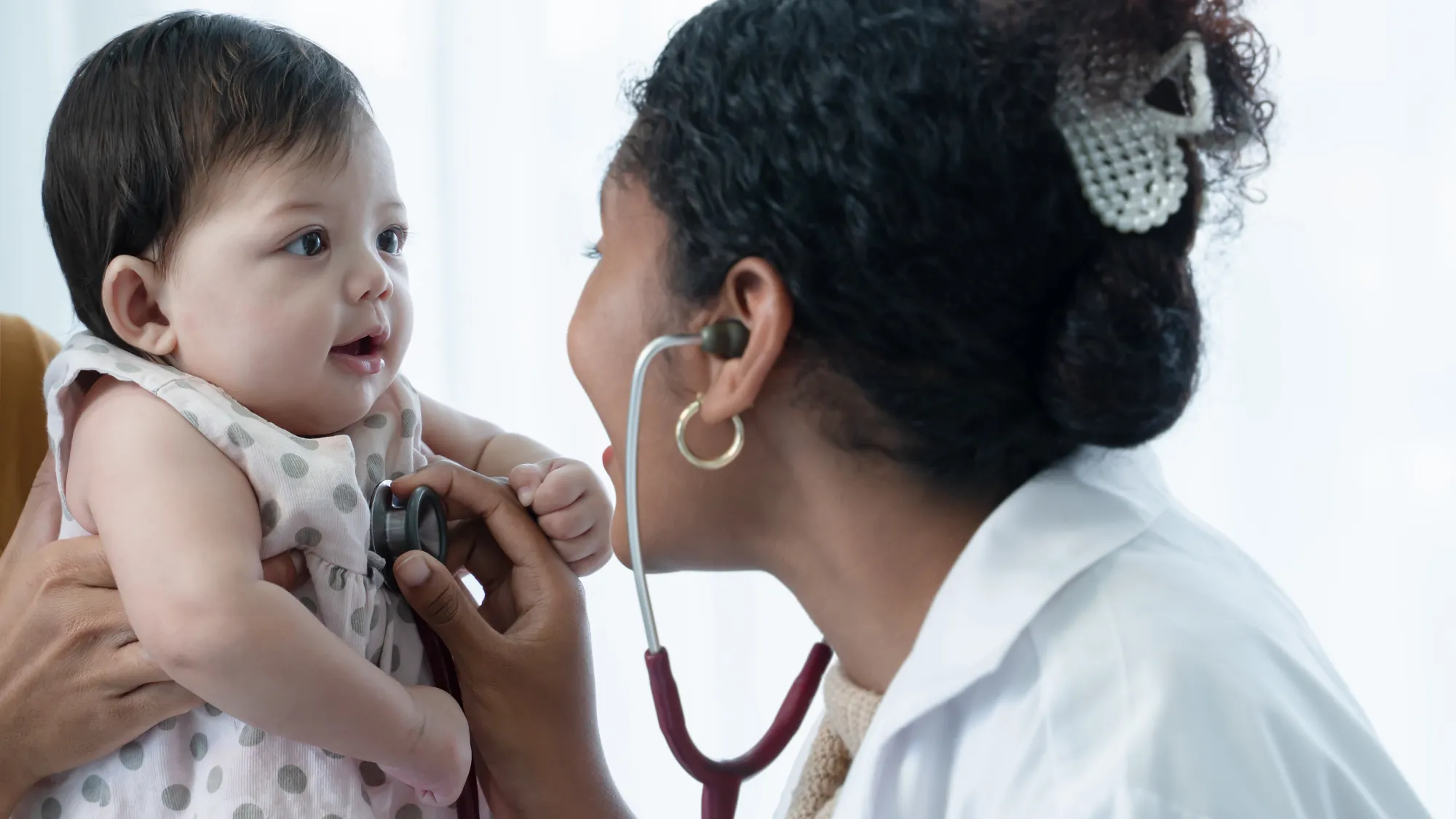 a smiling doctor taking the heartbeat of a one year old baby girl.