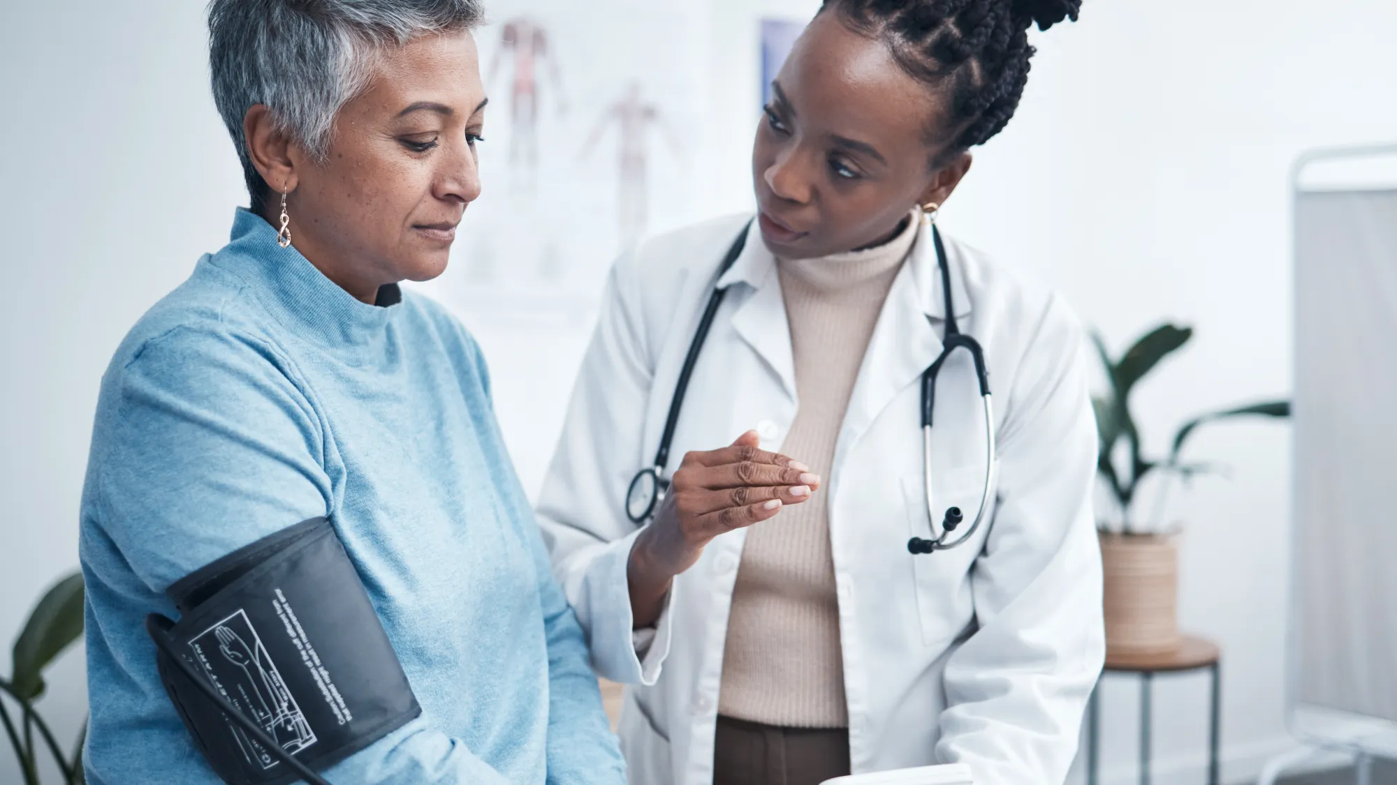 A female doctor wearing a white coat taking the blood pressure of a woman with gray hair.