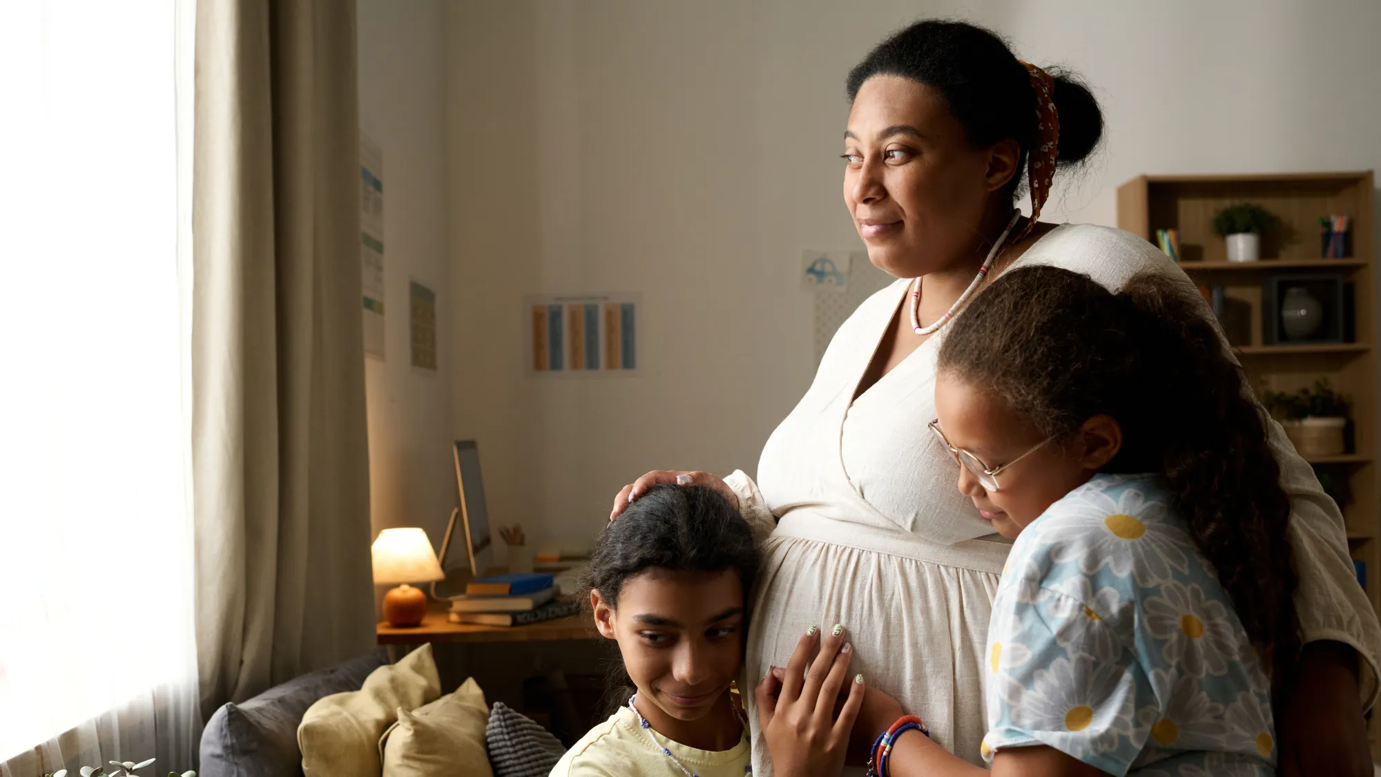 Pregnant woman hugging two of her children in their living room while
