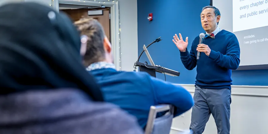 Gil Liu presents at a podium with a microphone in hand addressing the audience. 
