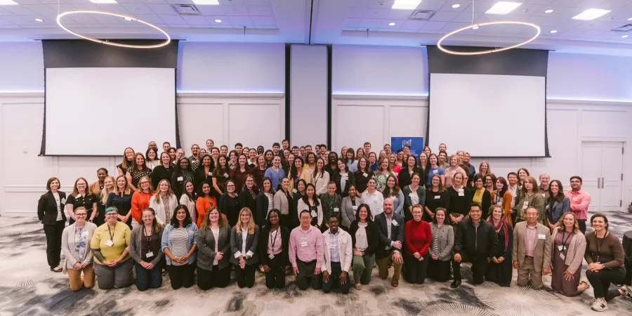 A group photo of nearly 130 staffers, some sitting and some standing smiling at the camera.