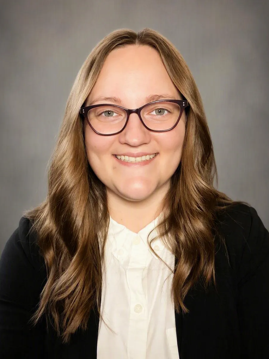 Woman with light brown hair and black glasses wearing business attire