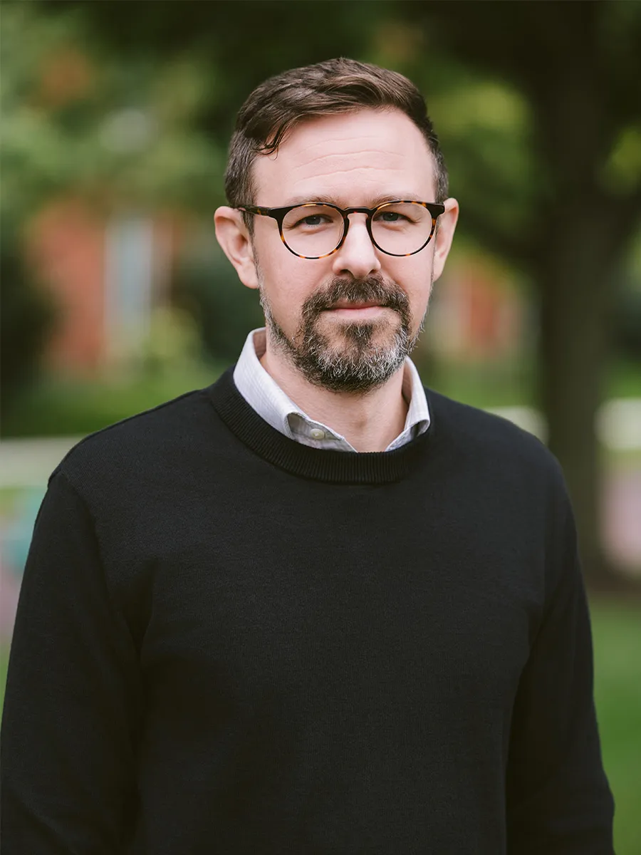 Headshot of Nate Doogan, a white male with glasses wearing a black sweater